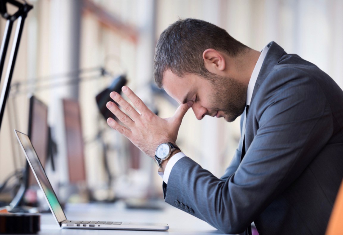 Man sitting exhausted with his hand on his forehead in front of his laptop – an image of the strain caused by conflict and separation
